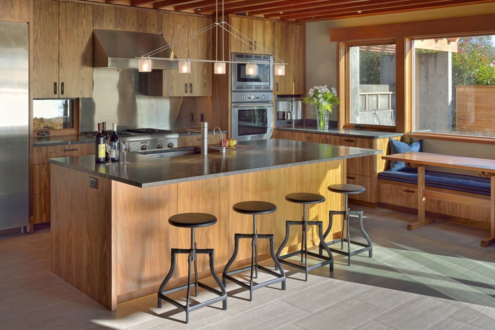 Foto på ett funkis l-kök, med en undermonterad diskho, släta luckor, skåp i mellenmörkt trä, stänkskydd med metallisk yta, rostfria vitvaror, en köksö och granitbänkskiva