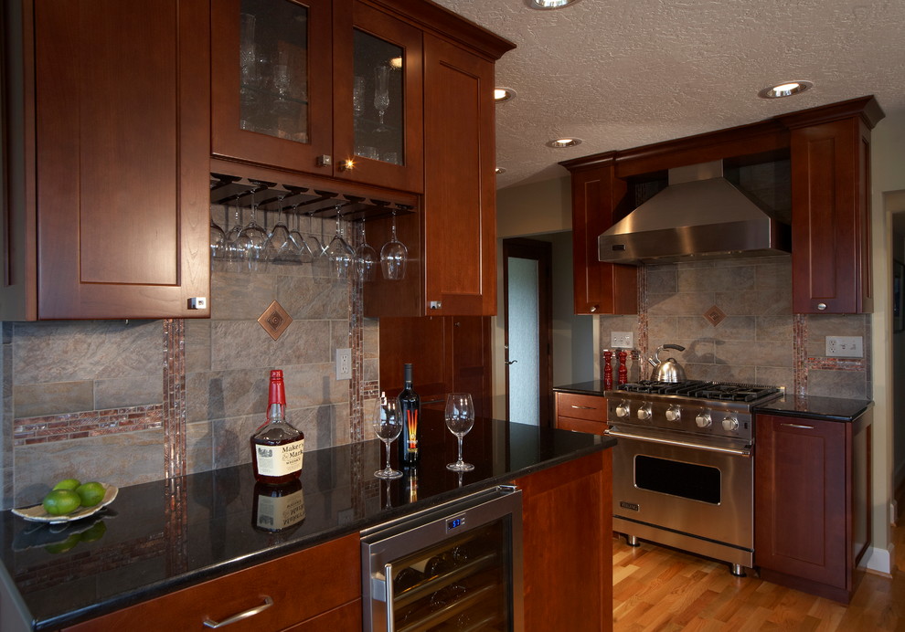 This is an example of a medium sized traditional l-shaped open plan kitchen in Seattle with a submerged sink, raised-panel cabinets, medium wood cabinets, granite worktops, metallic splashback, ceramic splashback, stainless steel appliances, light hardwood flooring, no island and beige floors.
