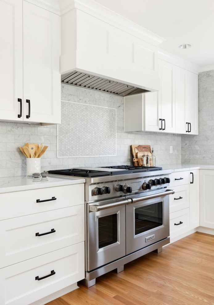 Foto de cocinas en L actual con armarios estilo shaker, electrodomésticos de acero inoxidable, suelo de madera clara, suelo marrón, encimeras blancas, puertas de armario blancas, encimera de cuarzo compacto, salpicadero verde, salpicadero de azulejos de vidrio y una isla