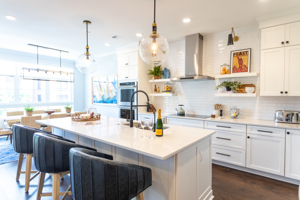 Example of a transitional galley dark wood floor and brown floor kitchen design in Baltimore with an undermount sink, shaker cabinets, white cabinets, white backsplash, subway tile backsplash, stainless steel appliances, an island and white countertops