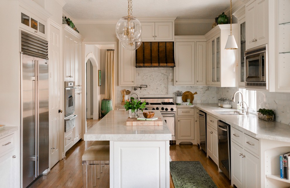 Geschlossene Klassische Küche in L-Form mit Doppelwaschbecken, profilierten Schrankfronten, weißen Schränken, Küchenrückwand in Grau, Küchengeräten aus Edelstahl, braunem Holzboden, Kücheninsel und grauer Arbeitsplatte in Houston