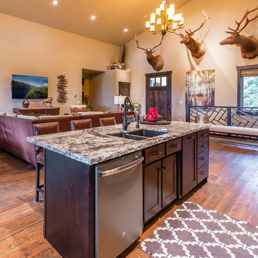 Rustic open plan kitchen in Other with a double-bowl sink, shaker cabinets, dark wood cabinets, granite worktops, stainless steel appliances, light hardwood flooring, an island and beige floors.
