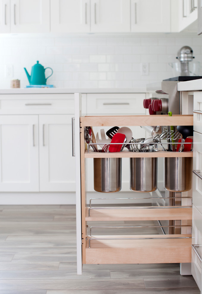 Large transitional l-shaped light wood floor eat-in kitchen photo in Vancouver with a farmhouse sink, shaker cabinets, white cabinets, solid surface countertops, white backsplash, subway tile backsplash, stainless steel appliances and an island