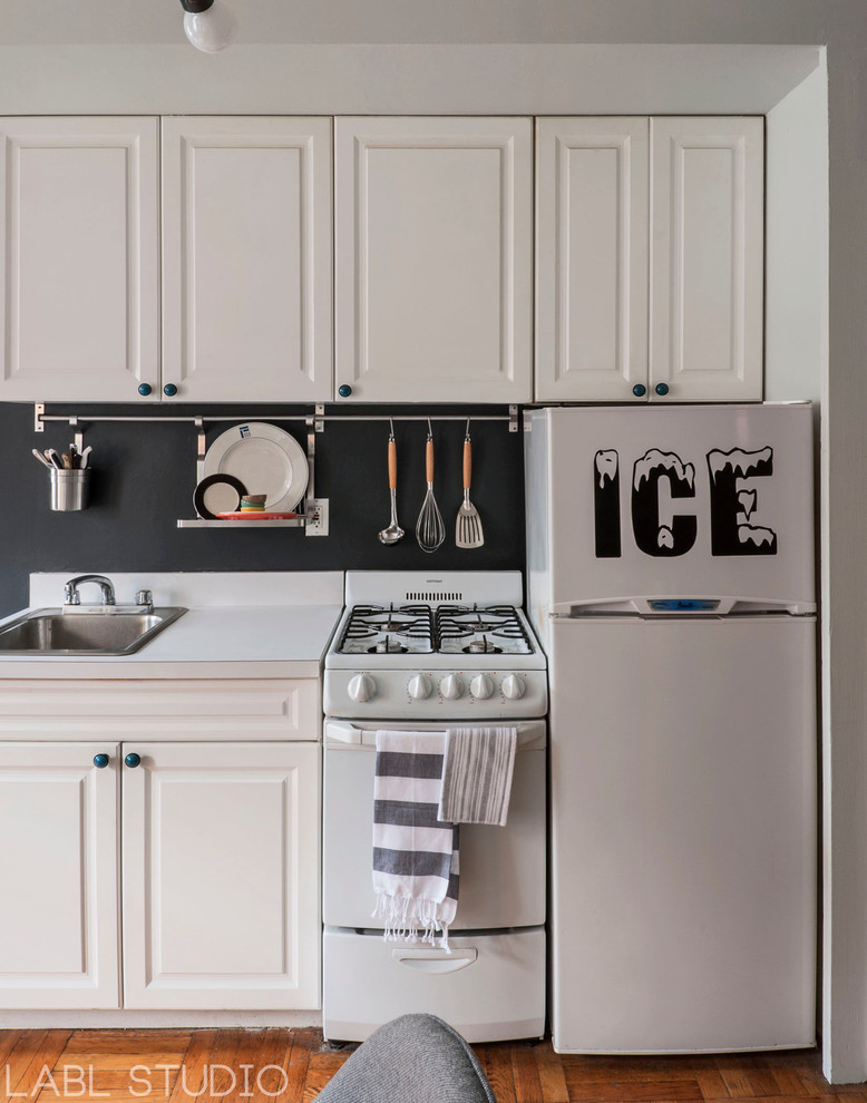 Mid-sized eclectic single-wall eat-in kitchen photo in New York with recessed-panel cabinets, white cabinets and black backsplash