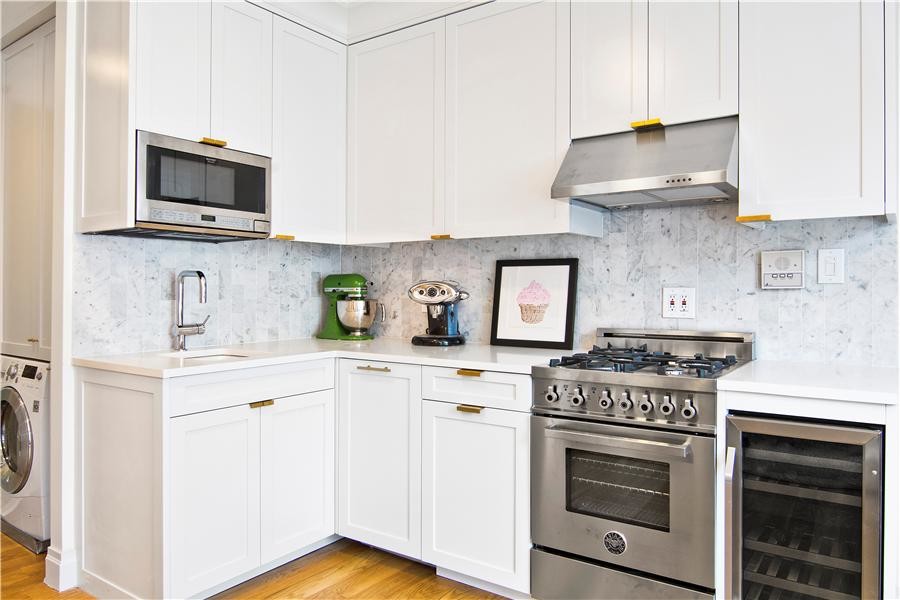 Eat-in kitchen - large modern l-shaped light wood floor eat-in kitchen idea in New York with shaker cabinets, white cabinets, granite countertops, white backsplash, stone tile backsplash, stainless steel appliances, no island and an undermount sink