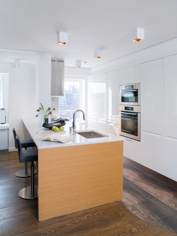 Immagine di un cucina con isola centrale contemporaneo con lavello sottopiano, ante lisce, ante bianche, elettrodomestici in acciaio inossidabile, pavimento marrone e top bianco