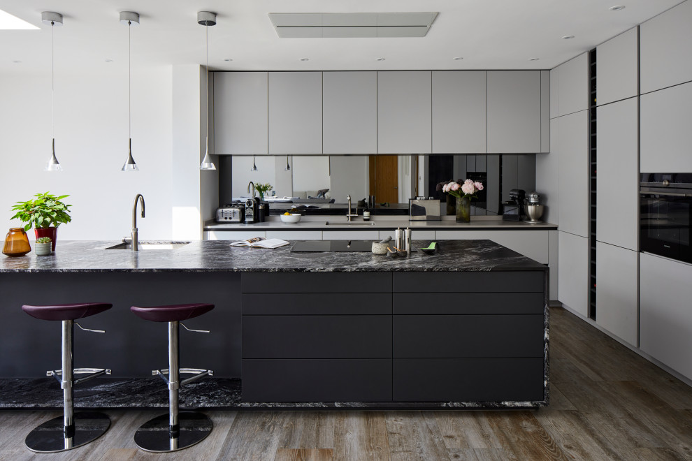 This is an example of a large contemporary l-shaped kitchen/diner in Kent with flat-panel cabinets, grey cabinets, granite worktops, mirror splashback, stainless steel appliances, an island and black worktops.
