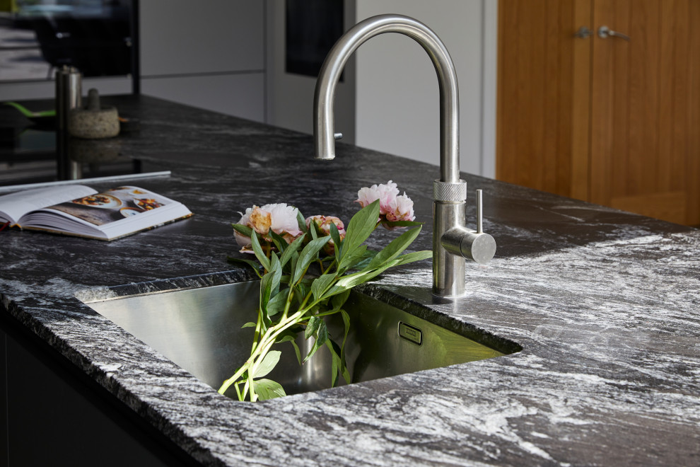 Foto di una grande cucina minimal con ante lisce, ante grigie, top in granito, paraspruzzi a specchio, elettrodomestici in acciaio inossidabile e top nero