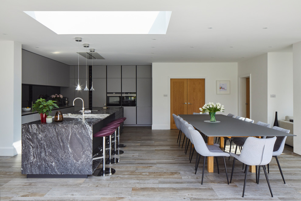 Große Moderne Wohnküche in L-Form mit flächenbündigen Schrankfronten, grauen Schränken, Granit-Arbeitsplatte, Rückwand aus Spiegelfliesen, Küchengeräten aus Edelstahl, Kücheninsel und schwarzer Arbeitsplatte in Kent