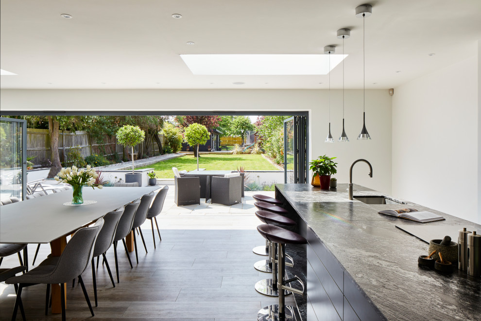 Large contemporary l-shaped kitchen/diner in Kent with flat-panel cabinets, grey cabinets, granite worktops, mirror splashback, stainless steel appliances, an island and black worktops.