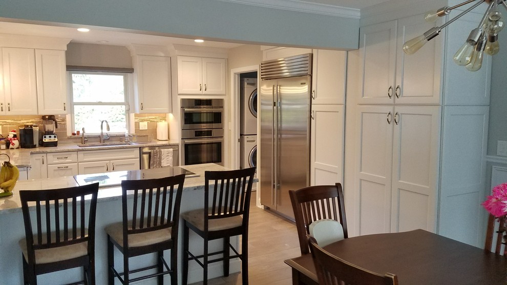Bild på ett mellanstort vintage kök, med en undermonterad diskho, luckor med infälld panel, vita skåp, granitbänkskiva, grått stänkskydd, stänkskydd i glaskakel, rostfria vitvaror, mellanmörkt trägolv, en halv köksö och brunt golv