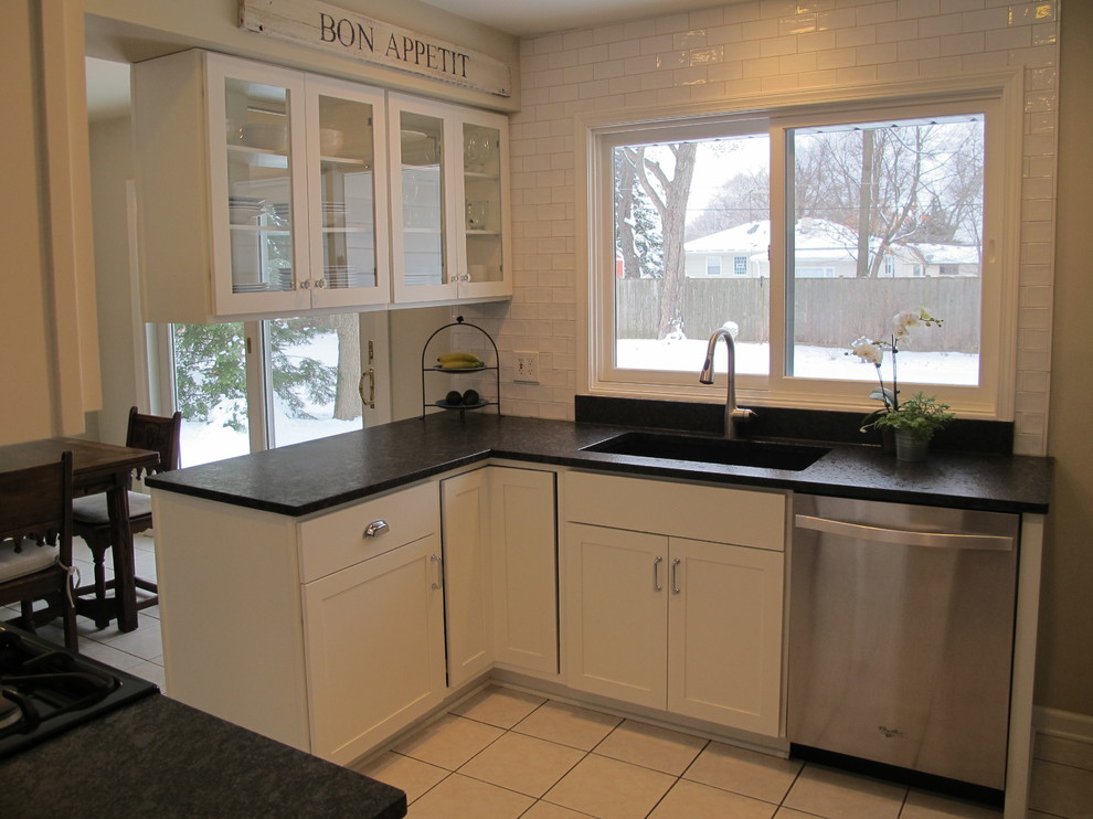 Klassisk inredning av ett litet svart svart kök och matrum, med en undermonterad diskho, skåp i shakerstil, vita skåp, granitbänkskiva, vitt stänkskydd, stänkskydd i keramik, rostfria vitvaror, klinkergolv i porslin, en halv köksö och beiget golv