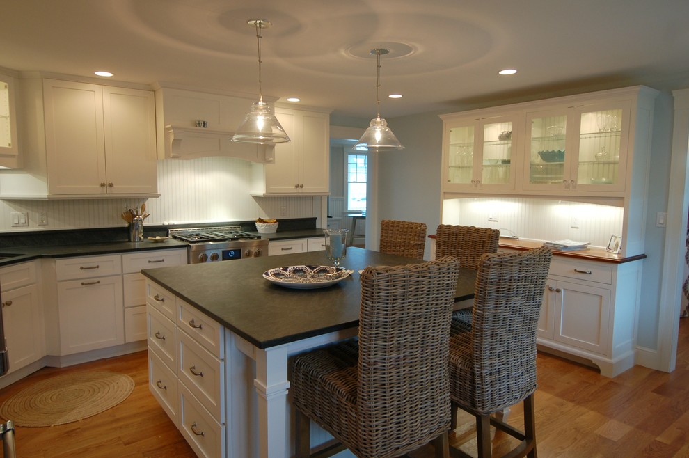 Example of a mid-sized beach style medium tone wood floor kitchen design in Boston with an undermount sink, recessed-panel cabinets, white cabinets, granite countertops, white backsplash, stainless steel appliances and an island