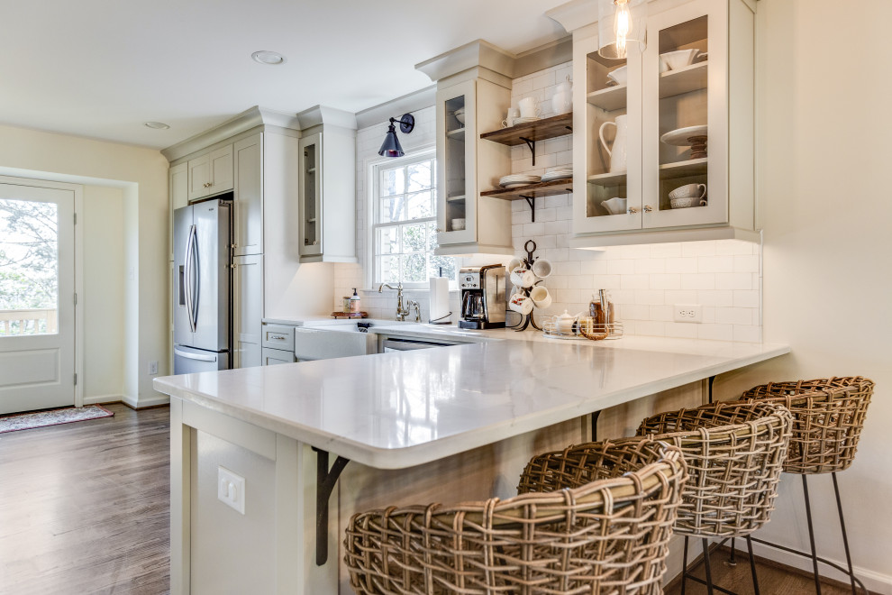 Example of a mid-sized transitional galley medium tone wood floor and brown floor eat-in kitchen design in Birmingham with a farmhouse sink, shaker cabinets, gray cabinets, quartz countertops, white backsplash, subway tile backsplash, stainless steel appliances, a peninsula and white countertops