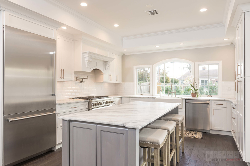 Large u-shaped plywood floor eat-in kitchen photo in New York with a farmhouse sink, recessed-panel cabinets, white cabinets, quartzite countertops, white backsplash, ceramic backsplash, stainless steel appliances and an island