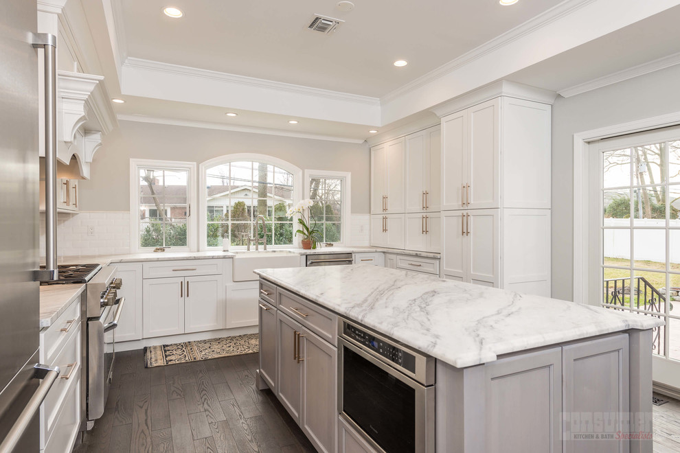 Large u-shaped plywood floor eat-in kitchen photo in New York with a farmhouse sink, recessed-panel cabinets, white cabinets, quartzite countertops, white backsplash, ceramic backsplash, stainless steel appliances and an island