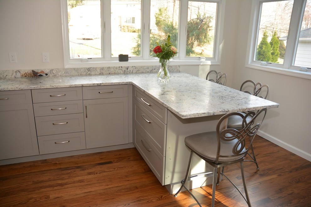 Example of a mid-sized transitional l-shaped medium tone wood floor eat-in kitchen design in New York with recessed-panel cabinets, gray cabinets, granite countertops, gray backsplash, glass tile backsplash and a peninsula