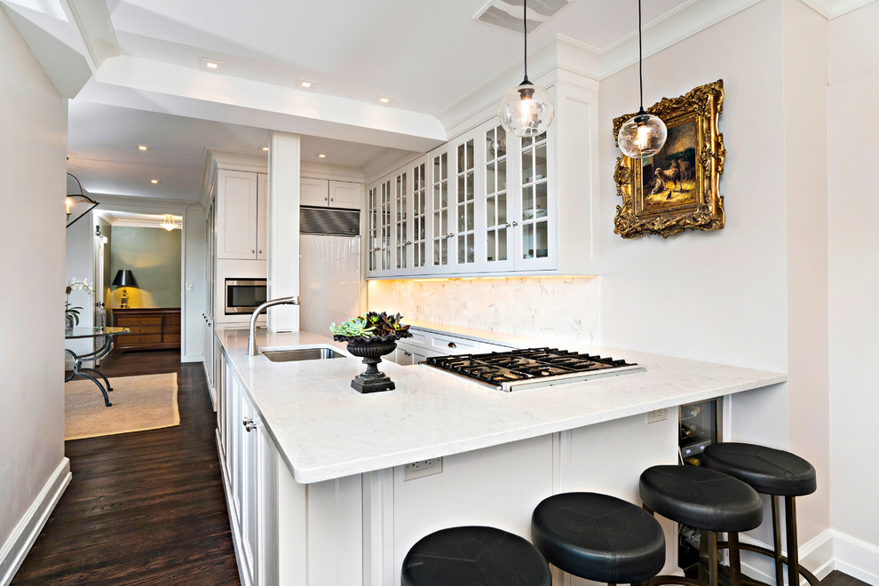 Small classic u-shaped kitchen in New York with a built-in sink, glass-front cabinets, white cabinets, white splashback, stainless steel appliances, dark hardwood flooring and an island.