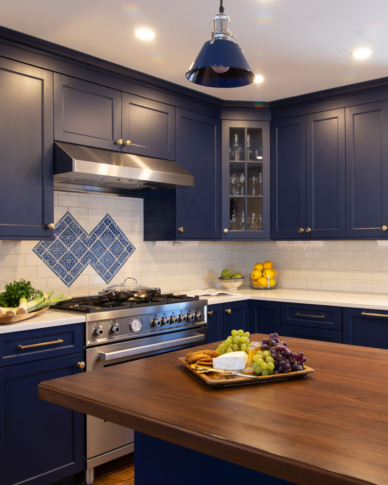 This is an example of a medium sized traditional l-shaped kitchen in New York with a belfast sink, shaker cabinets, blue cabinets, composite countertops, white splashback, metro tiled splashback, stainless steel appliances, light hardwood flooring, multiple islands and white worktops.