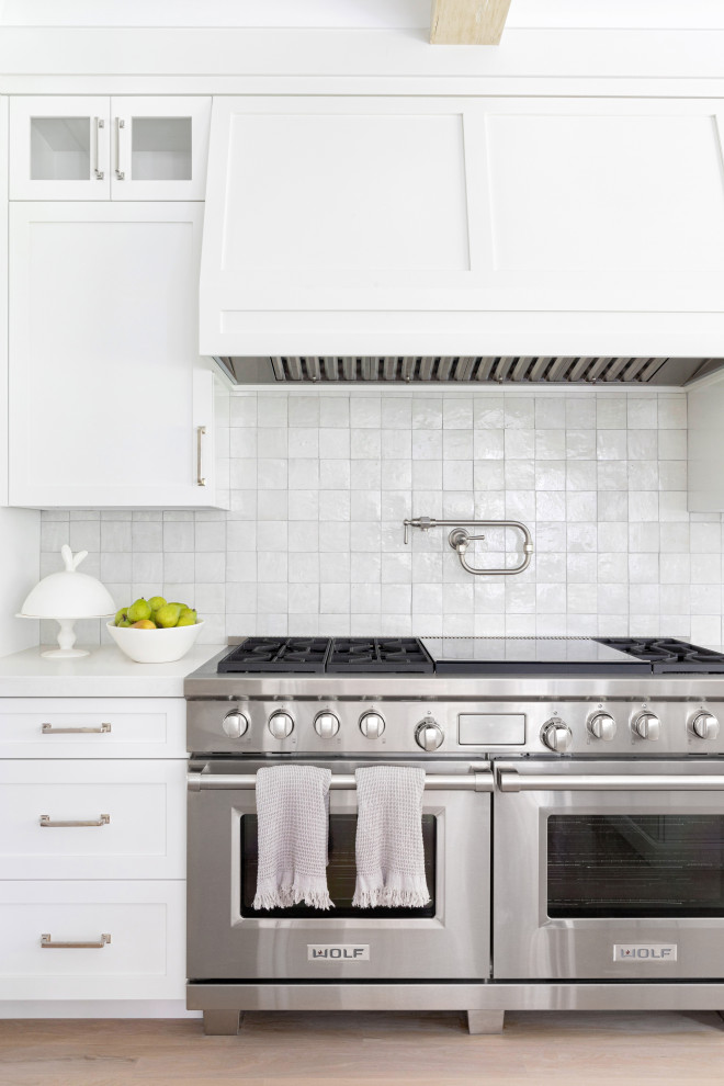 ニューヨークにあるラグジュアリーな広いトラディショナルスタイルのおしゃれなキッチン (エプロンフロントシンク、落し込みパネル扉のキャビネット、白いキャビネット、大理石カウンター、白いキッチンパネル、テラコッタタイルのキッチンパネル、シルバーの調理設備、淡色無垢フローリング、茶色い床、白いキッチンカウンター) の写真
