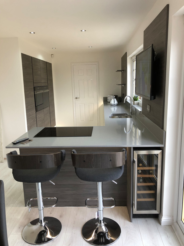 Photo of a medium sized contemporary l-shaped kitchen/diner in Glasgow with an integrated sink, flat-panel cabinets, grey cabinets, quartz worktops, brown splashback, wood splashback, stainless steel appliances, vinyl flooring, a breakfast bar, grey floors and grey worktops.