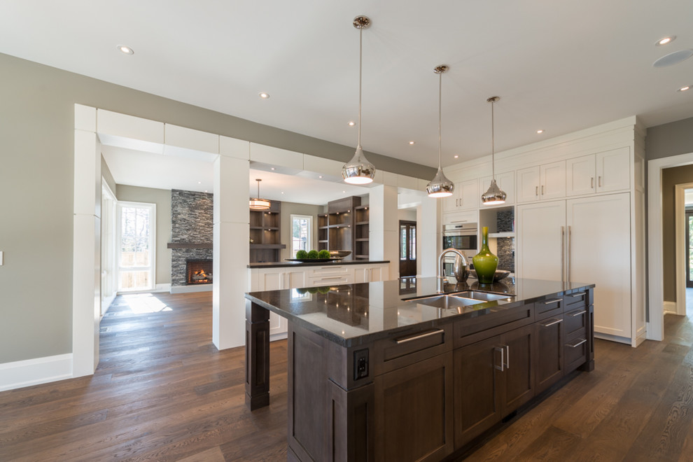 Inspiration for a large traditional l-shaped open plan kitchen in Toronto with a submerged sink, shaker cabinets, white cabinets, granite worktops, black splashback, mosaic tiled splashback, integrated appliances, medium hardwood flooring and an island.