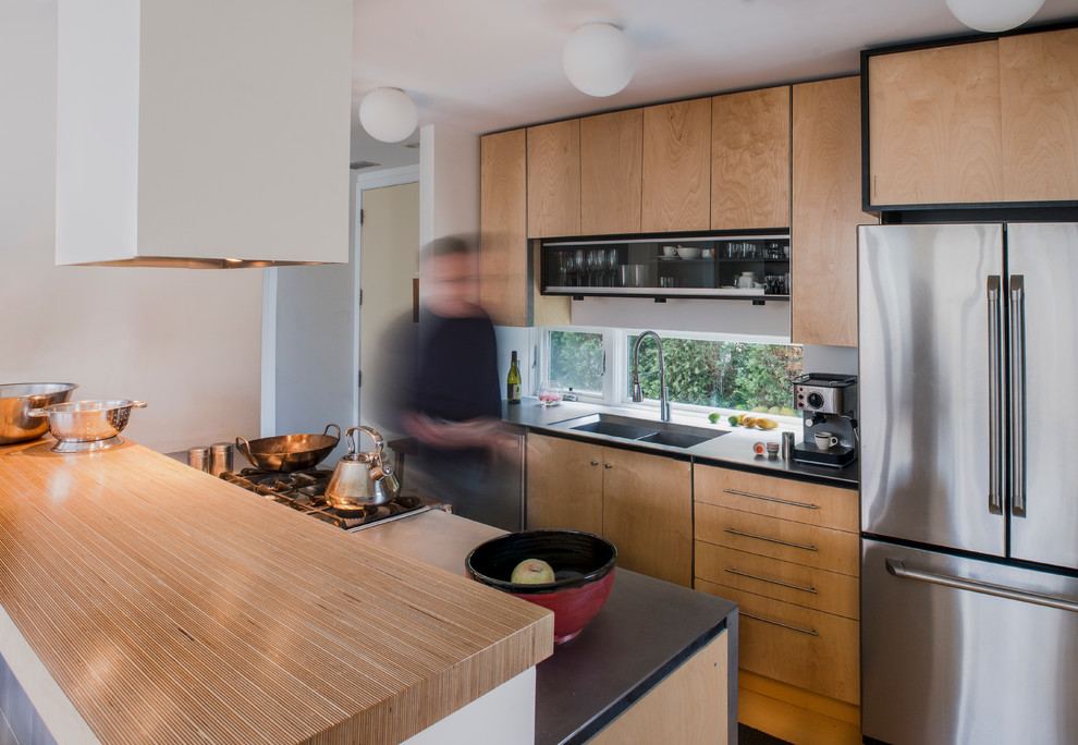 Пример оригинального дизайна: узкая параллельная кухня в современном стиле с врезной мойкой, плоскими фасадами, светлыми деревянными фасадами, техникой из нержавеющей стали и деревянной столешницей