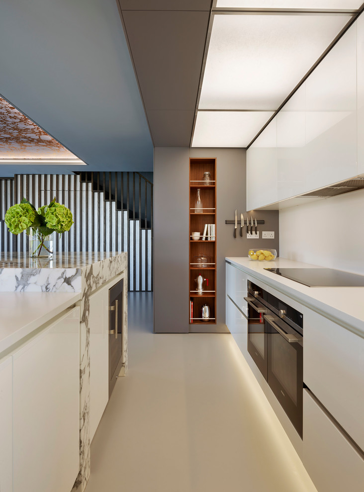 Foto på ett mycket stort funkis vit linjärt kök med öppen planlösning, med släta luckor, vita skåp, marmorbänkskiva, vitt stänkskydd, stänkskydd i sten, svarta vitvaror, en köksö och grått golv