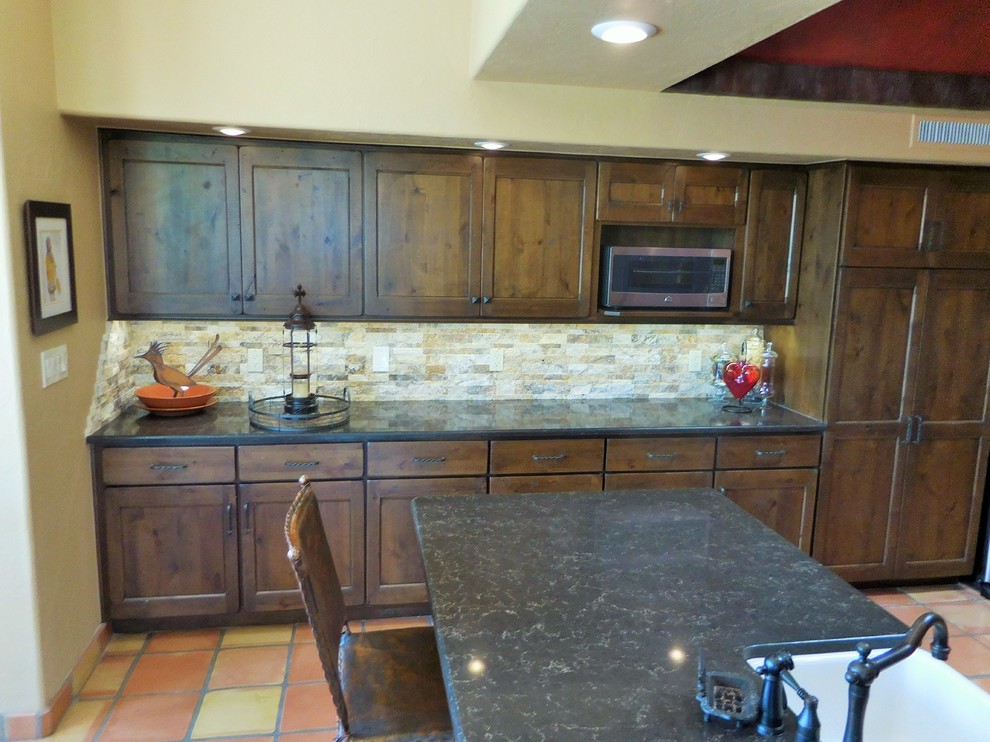 Example of a small southwest terra-cotta tile enclosed kitchen design in Phoenix with a farmhouse sink, shaker cabinets, brown cabinets, quartz countertops, beige backsplash, stone tile backsplash, stainless steel appliances and an island