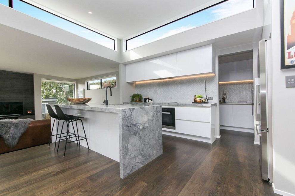 Inredning av ett modernt stort kök, med en undermonterad diskho, vita skåp, granitbänkskiva, grått stänkskydd, stänkskydd i marmor, rostfria vitvaror, laminatgolv, en köksö och brunt golv