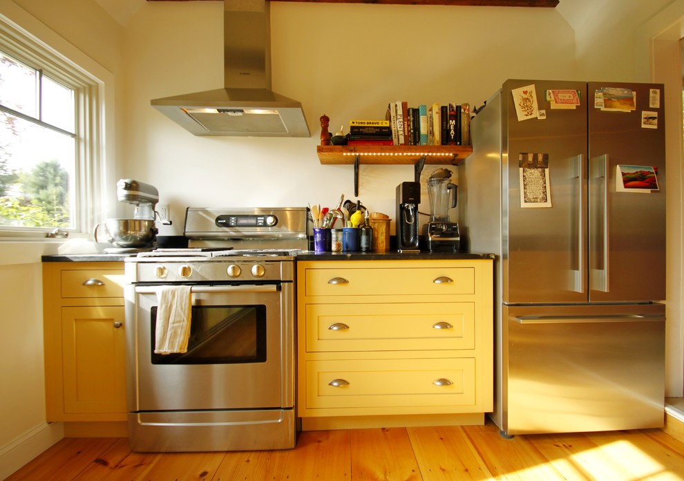 Foto på ett lantligt l-kök, med en integrerad diskho, luckor med infälld panel, gula skåp, bänkskiva i täljsten, stänkskydd i sten, rostfria vitvaror och ljust trägolv