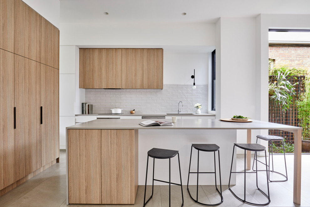Moderne Küche in L-Form mit Unterbauwaschbecken, flächenbündigen Schrankfronten, hellen Holzschränken, Küchenrückwand in Grau, Elektrogeräten mit Frontblende, Kücheninsel, grauem Boden und grauer Arbeitsplatte in Melbourne