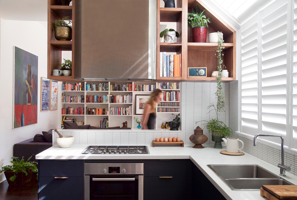 На фото: угловая, отдельная кухня в современном стиле с двойной мойкой, плоскими фасадами, синими фасадами, белым фартуком, фартуком из удлиненной плитки и техникой из нержавеющей стали