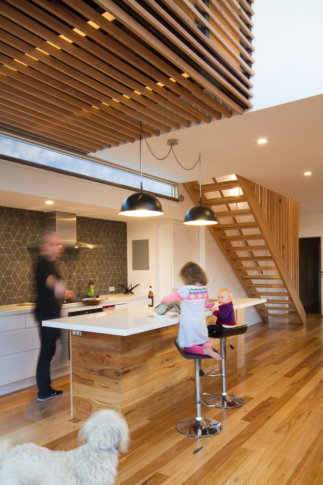 Imagen de cocina actual abierta con salpicadero verde, suelo de madera en tonos medios y una isla