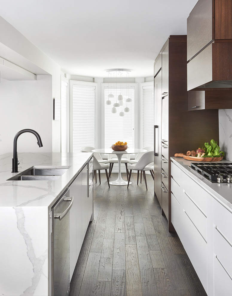 Inspiration for an expansive contemporary galley open plan kitchen in Toronto with a submerged sink, flat-panel cabinets, dark wood cabinets, engineered stone countertops, white splashback, stone slab splashback, integrated appliances, dark hardwood flooring, an island and white worktops.