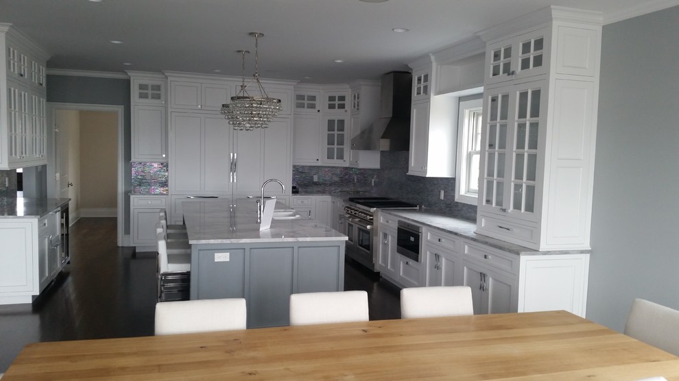 Photo of a traditional l-shaped kitchen/diner in New York with a belfast sink, recessed-panel cabinets, grey cabinets, quartz worktops, multi-coloured splashback, ceramic splashback, integrated appliances, dark hardwood flooring and an island.