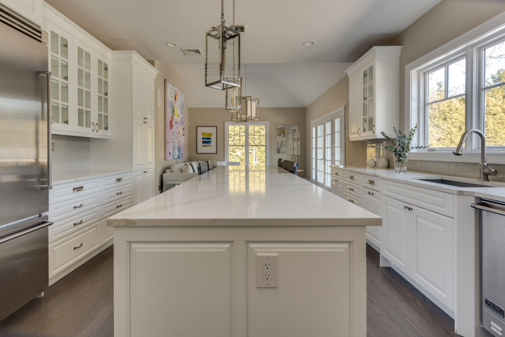 Foto på ett funkis vit kök, med en undermonterad diskho, släta luckor, vita skåp, marmorbänkskiva, beige stänkskydd, stänkskydd i glaskakel, rostfria vitvaror, mellanmörkt trägolv och en köksö