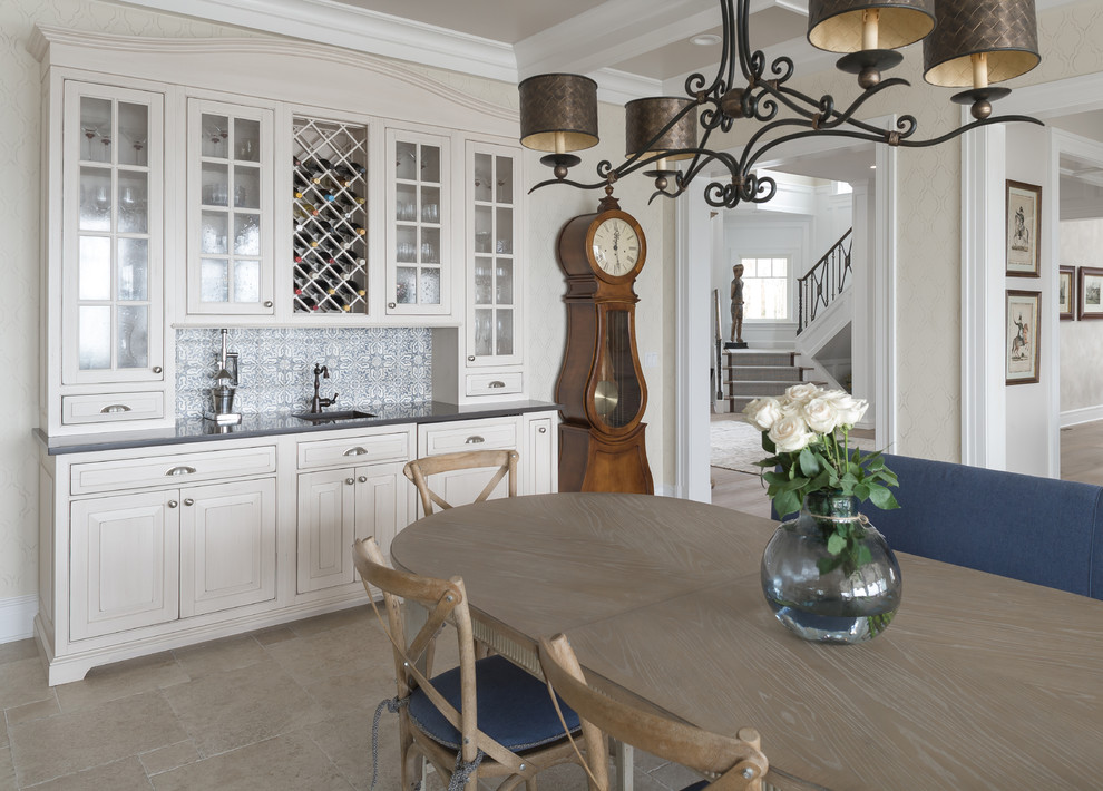 Klassisk inredning av ett stort kök, med en rustik diskho, luckor med infälld panel, vita skåp, granitbänkskiva, brunt stänkskydd, stänkskydd i cementkakel, rostfria vitvaror, kalkstensgolv och en köksö