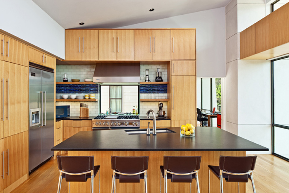 This is an example of a contemporary l-shaped kitchen/diner in Austin with a submerged sink, flat-panel cabinets, light wood cabinets, composite countertops, white splashback, metro tiled splashback, light hardwood flooring and an island.