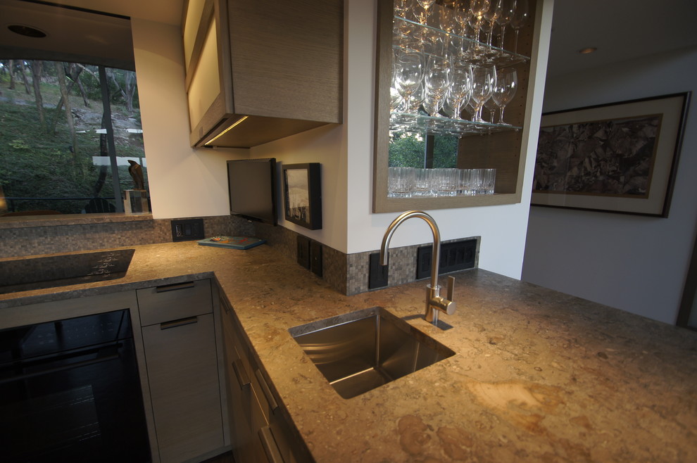 Inspiration for a mid-sized modern u-shaped cork floor enclosed kitchen remodel in Austin with a single-bowl sink, flat-panel cabinets, gray cabinets, limestone countertops, multicolored backsplash, mosaic tile backsplash, paneled appliances and an island
