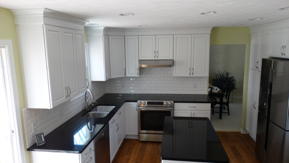 Inspiration for a mid-sized timeless u-shaped light wood floor eat-in kitchen remodel in Cleveland with an undermount sink, raised-panel cabinets, white cabinets, granite countertops, white backsplash, ceramic backsplash, stainless steel appliances and an island