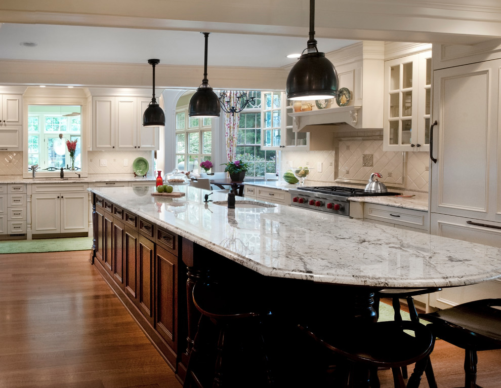 Example of a large classic u-shaped medium tone wood floor eat-in kitchen design in Cleveland with an undermount sink, recessed-panel cabinets, white cabinets, granite countertops, beige backsplash, ceramic backsplash, paneled appliances and an island