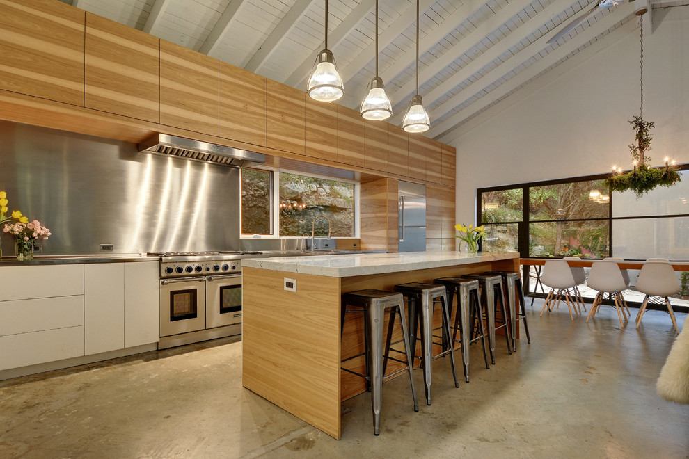 Inspiration för ett stort eklektiskt linjärt kök med öppen planlösning, med släta luckor, skåp i ljust trä, en köksö, bänkskiva i rostfritt stål, stänkskydd med metallisk yta, stänkskydd i metallkakel, rostfria vitvaror, en integrerad diskho och betonggolv