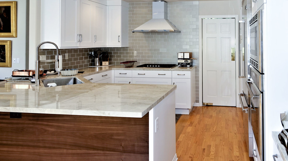 Inredning av ett industriellt mellanstort vit vitt kök, med en undermonterad diskho, skåp i shakerstil, vita skåp, bänkskiva i kvarts, grått stänkskydd, stänkskydd i tunnelbanekakel, rostfria vitvaror, mellanmörkt trägolv, en halv köksö och brunt golv