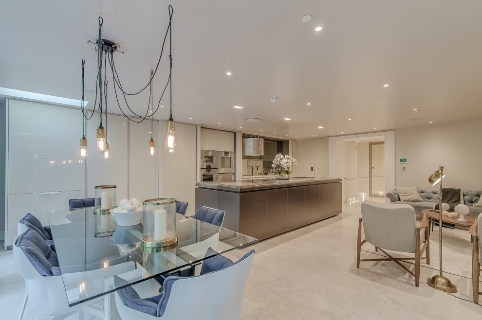 Inspiration for an expansive traditional galley kitchen/diner in London with a built-in sink, flat-panel cabinets, beige cabinets, marble worktops, metallic splashback, mirror splashback, stainless steel appliances, marble flooring and an island.