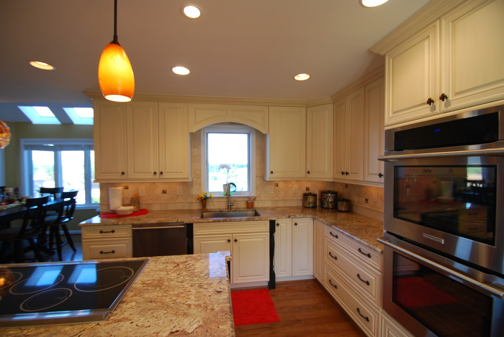 Inredning av ett klassiskt stort kök, med en undermonterad diskho, vita skåp, granitbänkskiva, beige stänkskydd, stänkskydd i stenkakel, rostfria vitvaror och en köksö