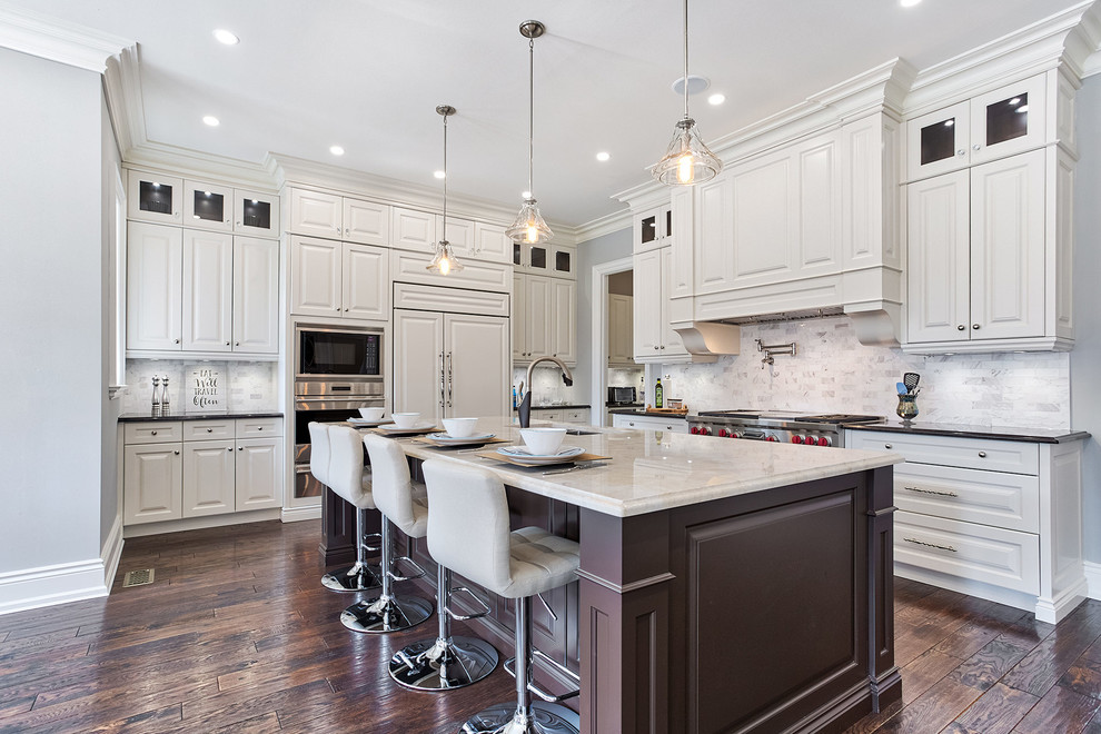 This is an example of a traditional kitchen in Toronto with raised-panel cabinets, an island, a submerged sink, white splashback, integrated appliances, dark hardwood flooring, brown floors, black worktops and beige cabinets.
