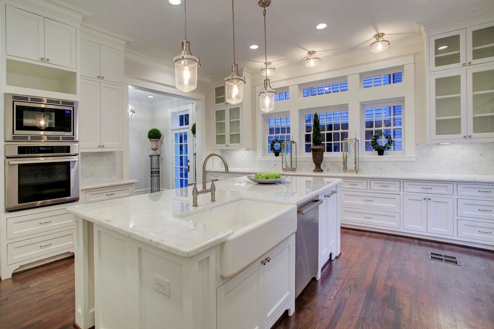 Photo of an expansive victorian l-shaped open plan kitchen in Houston with a belfast sink, flat-panel cabinets, marble worktops, white splashback, stone tiled splashback, stainless steel appliances, dark hardwood flooring and an island.