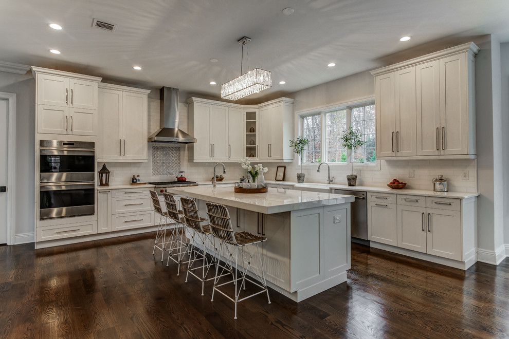 Inspiration for a large traditional u-shaped kitchen/diner in New York with a belfast sink, flat-panel cabinets, white cabinets, quartz worktops, white splashback, metro tiled splashback, stainless steel appliances, dark hardwood flooring, an island and brown floors.