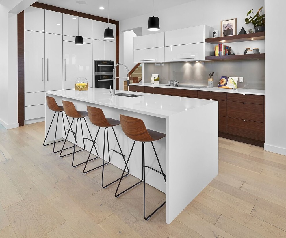 Modern inredning av ett stort kök, med en undermonterad diskho, luckor med profilerade fronter, vita skåp, bänkskiva i kvarts, stänkskydd med metallisk yta, stänkskydd i metallkakel, rostfria vitvaror, ljust trägolv, en köksö och brunt golv